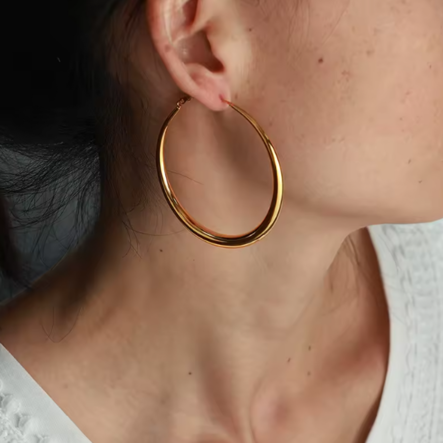Gold hoop earring worn by a person with a neutral background