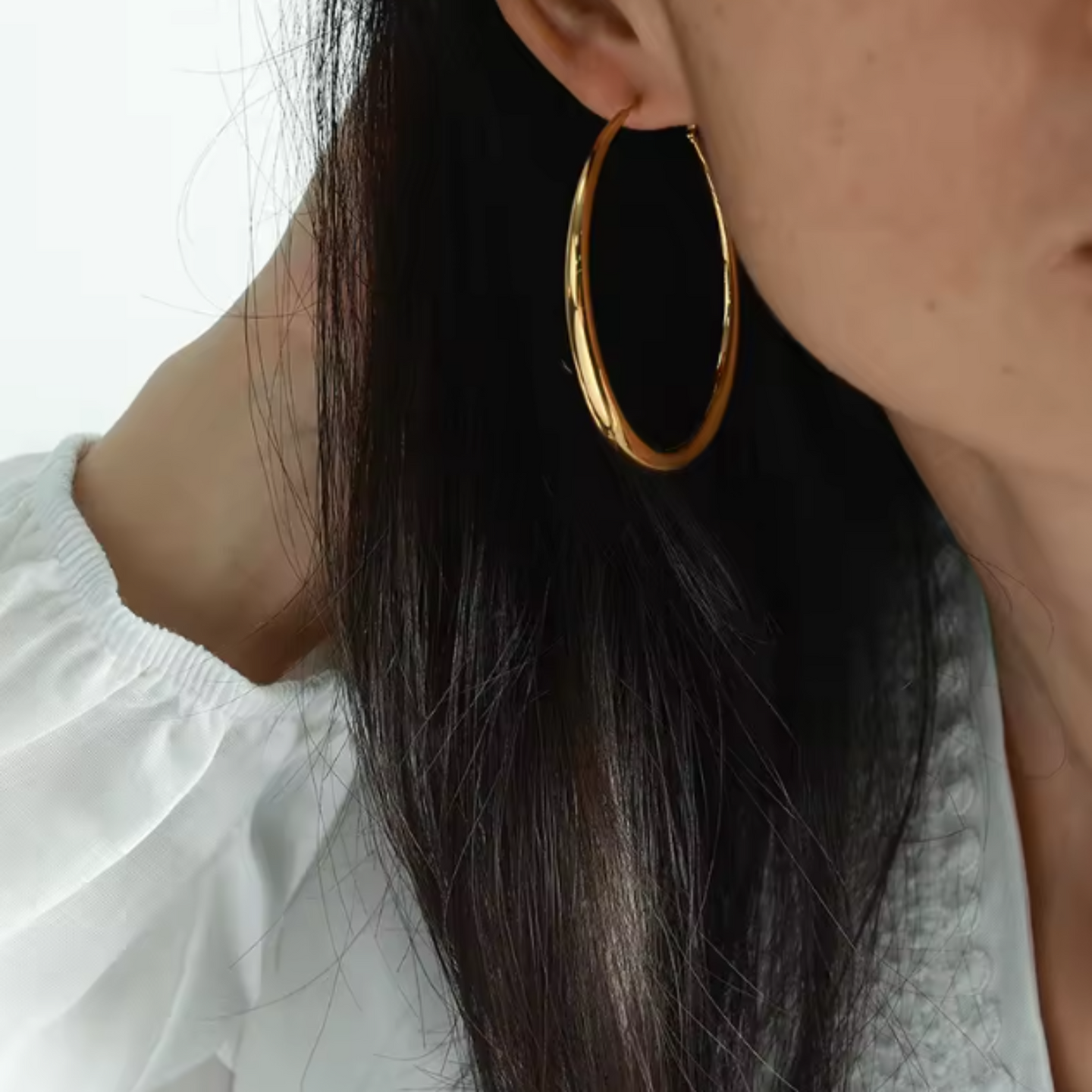 Close-up of a person wearing gold hoop earrings with a blurred background
