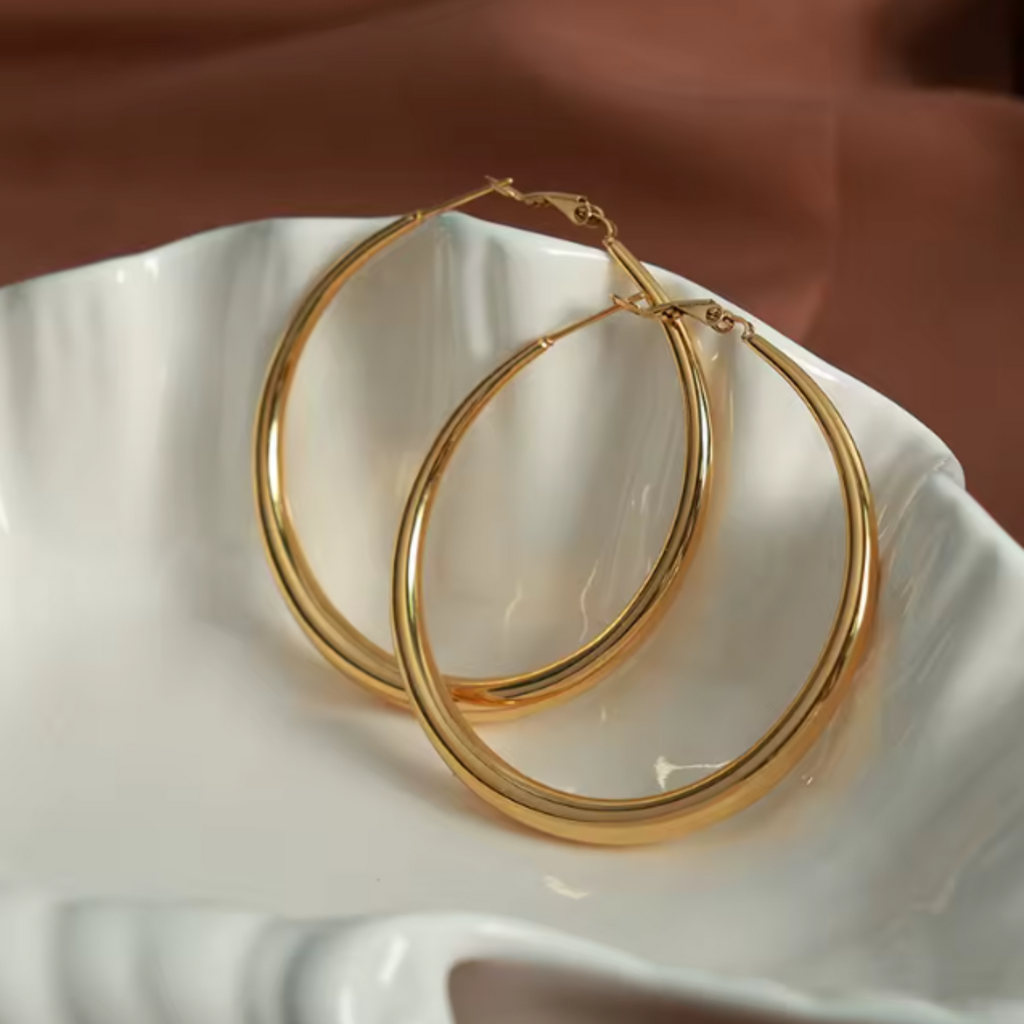 Gold hoop earrings on a white ceramic dish with a brown background