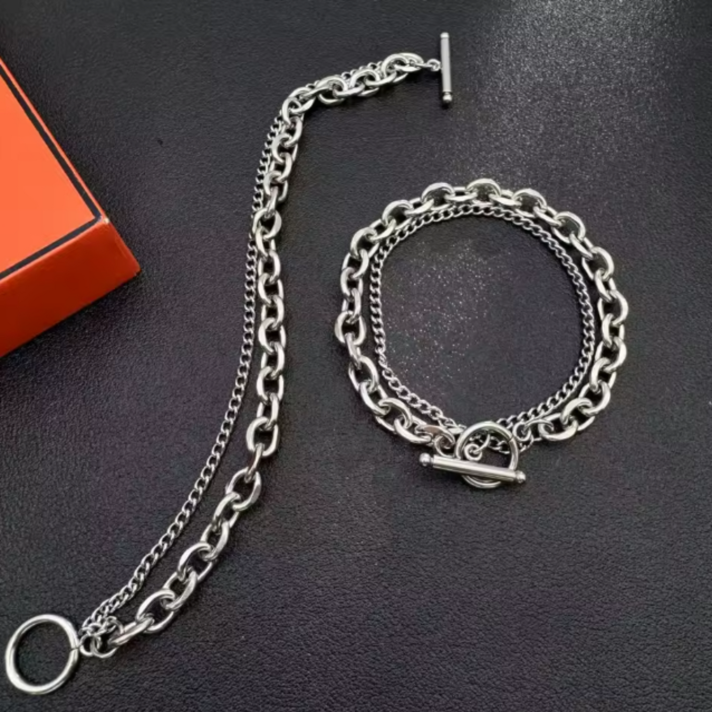 Silver chain necklace and bracelet on a dark surface with an orange box in the background.