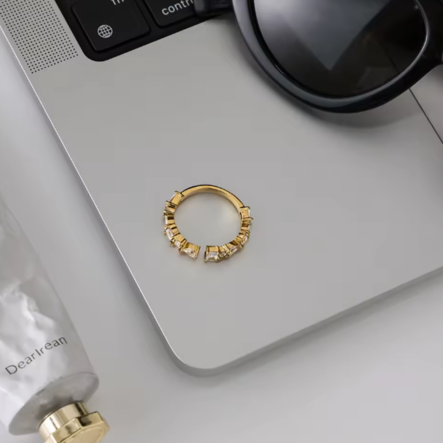 Gold hoop earring on a laptop keyboard with a bottle of skincare product.