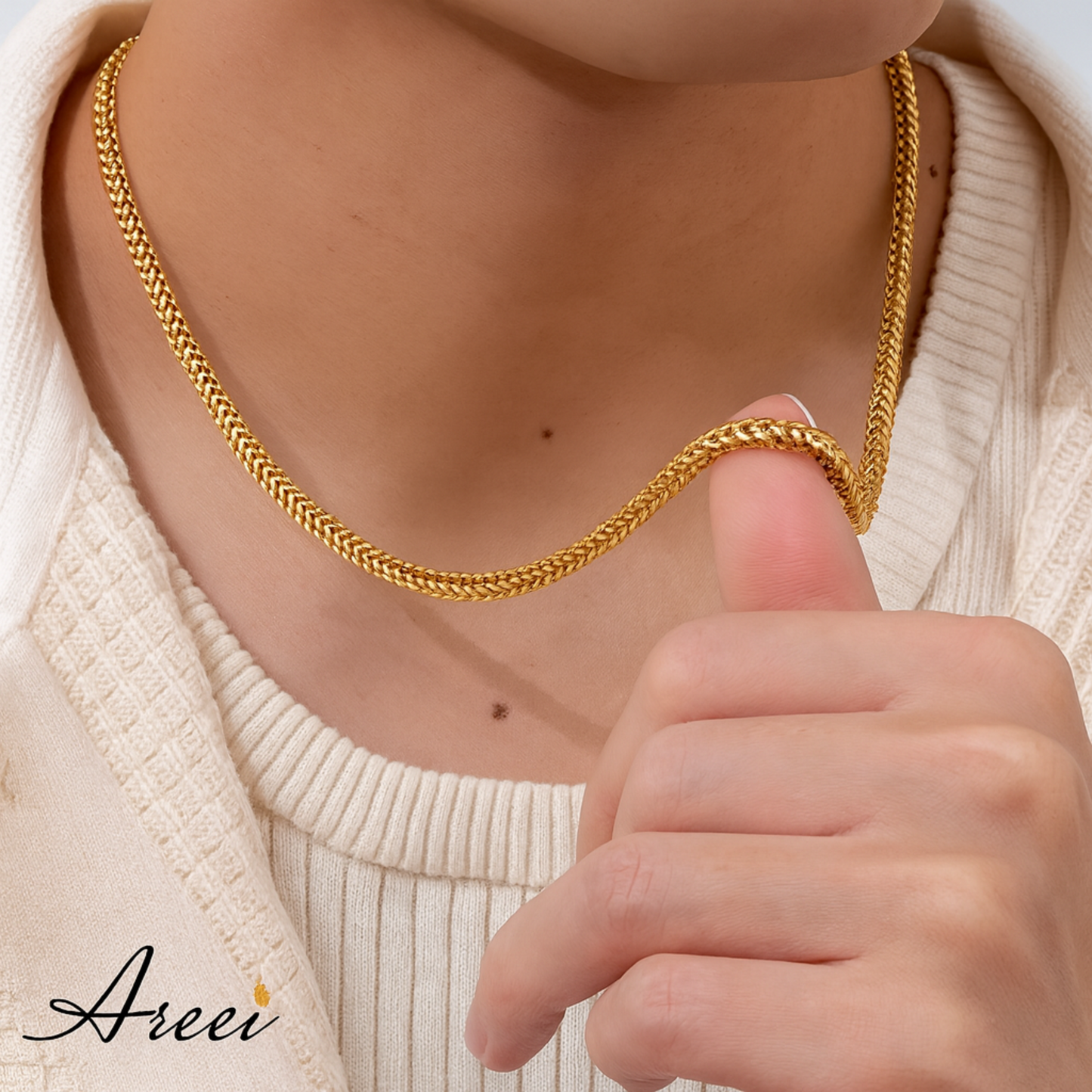 Gold chain necklace being held by a hand, with 'Areei' brand visible.