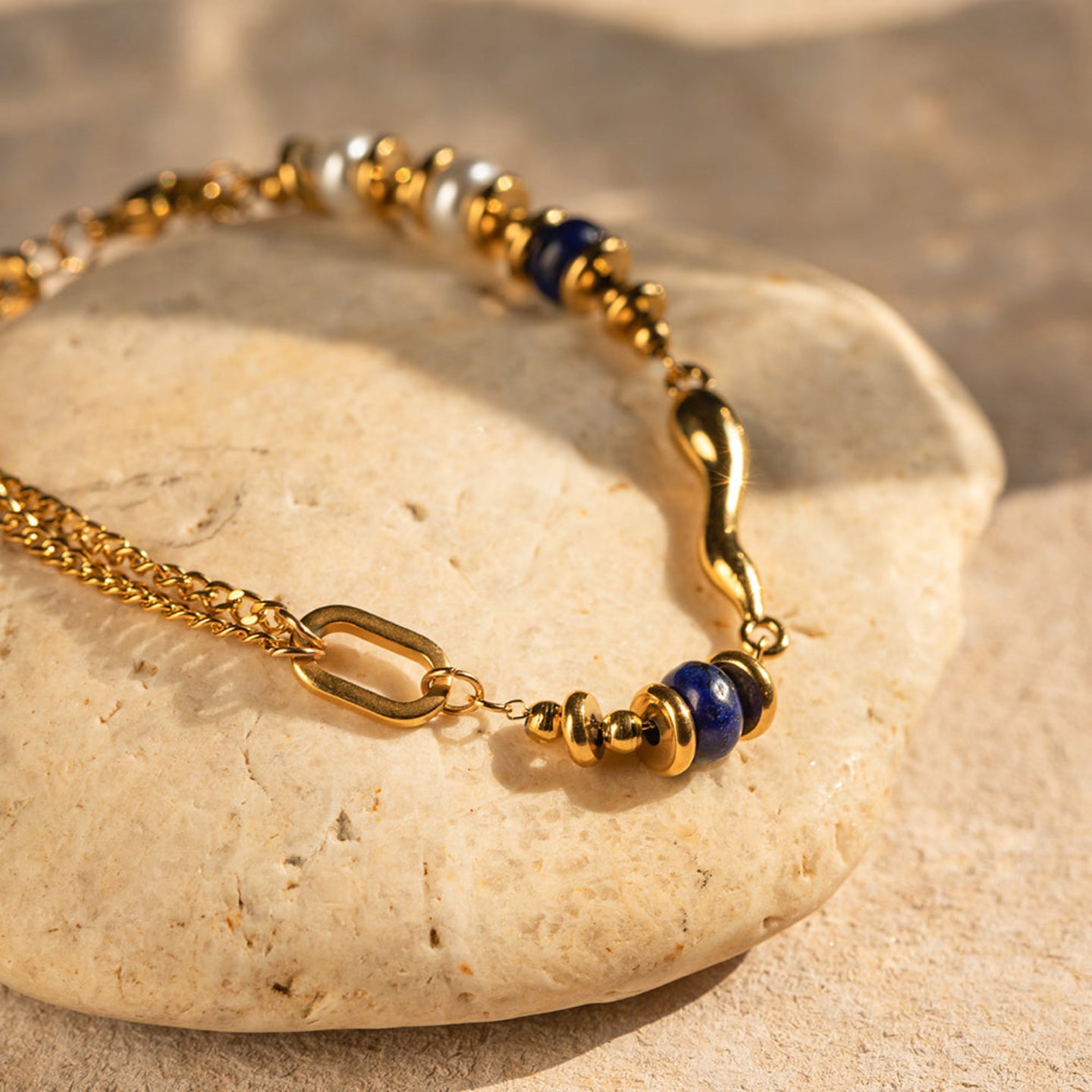 Gold bracelet with blue beads on a stone surface