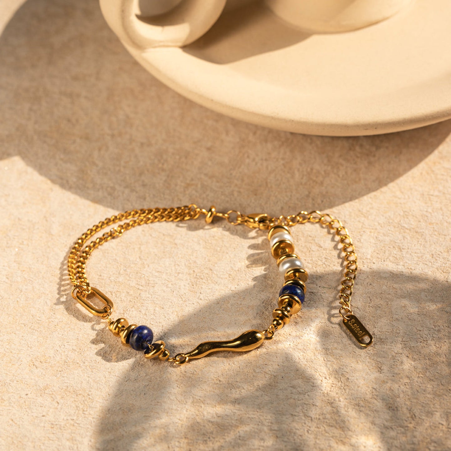 Gold bracelet with blue and white beads on a beige surface