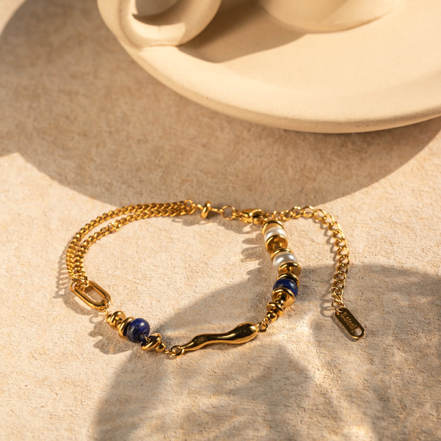 Gold bracelet with blue and white beads on a beige surface