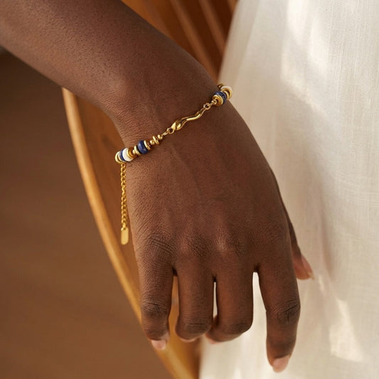 Gold bracelet with blue beads on a person's wrist against a neutral background