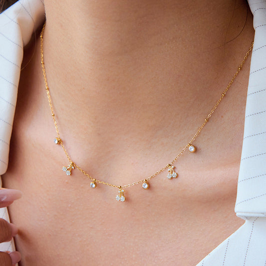 Gold necklace with small pendants on a person wearing a white shirt.