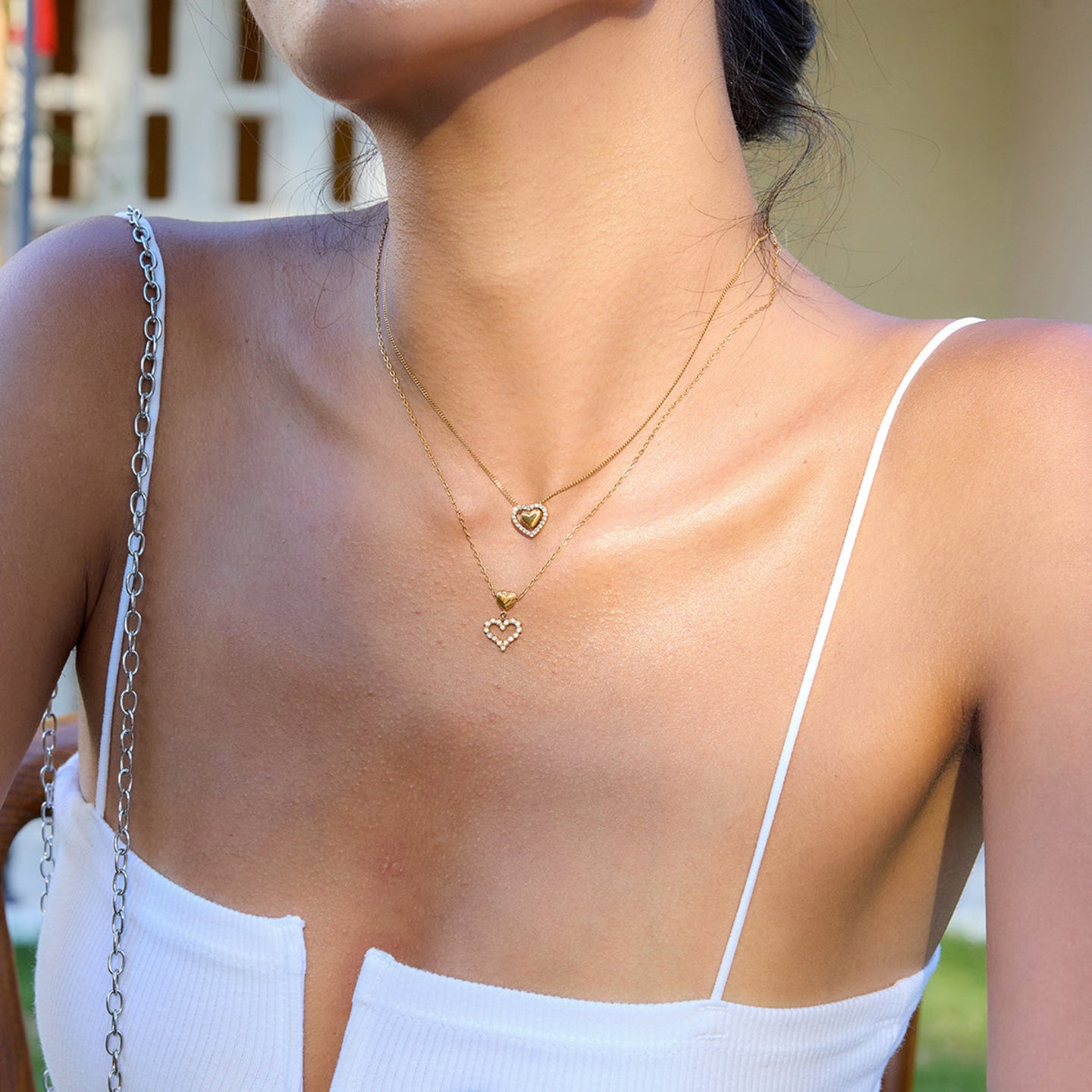 Close-up of a person wearing two gold heart-shaped necklaces with a blurred background