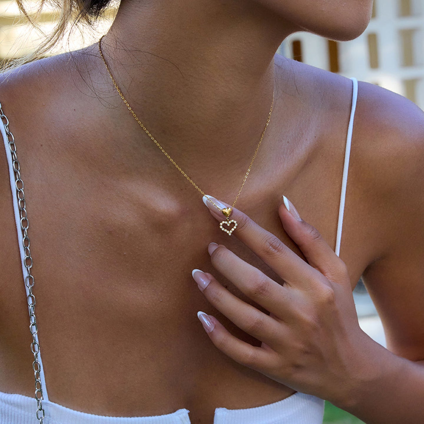 Woman wearing a gold necklace with a heart pendant, touching her chest.
